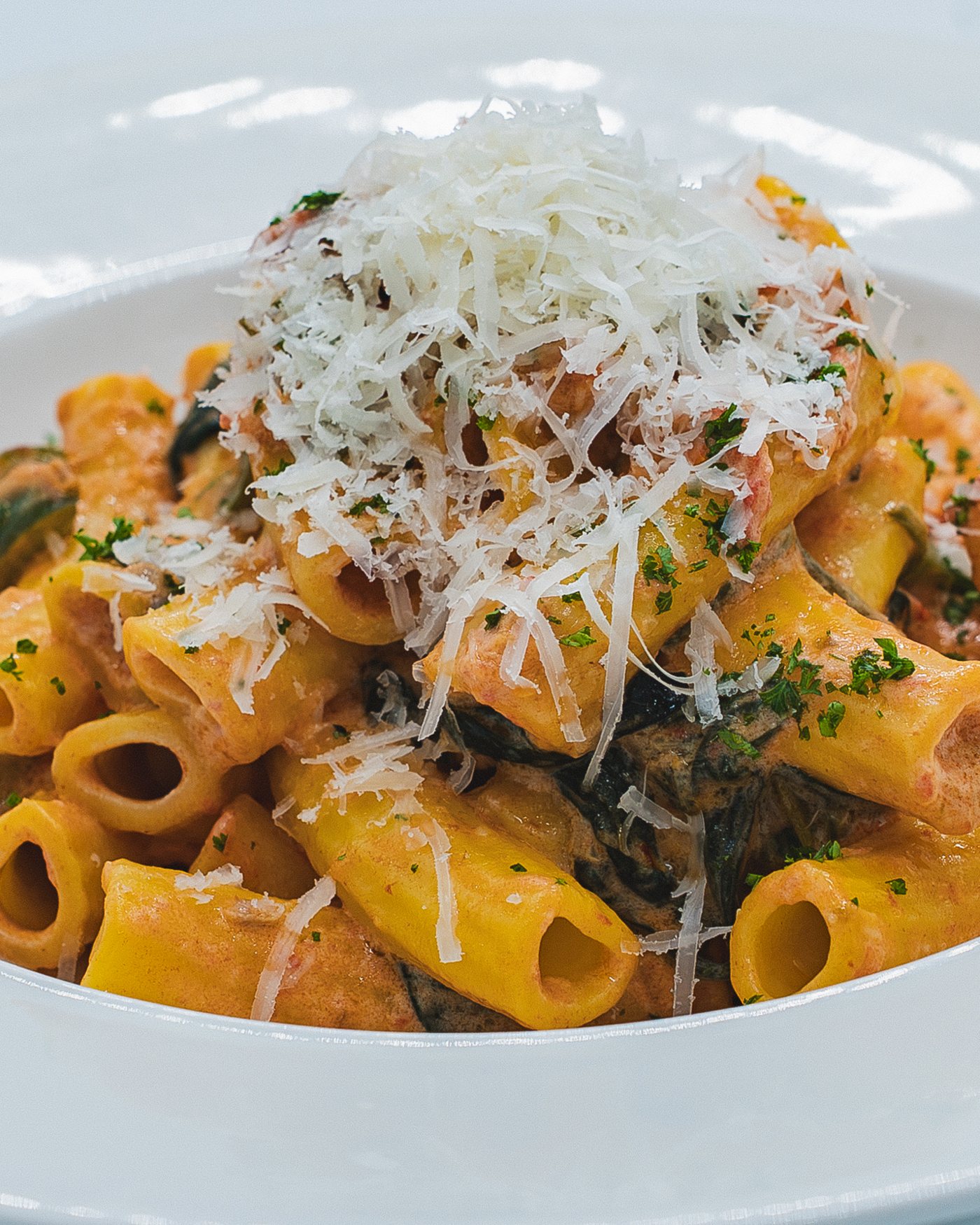 Rigatoni pasta in a saffron sauce with sun-blushed tomatoes and spinach, topped with grated parmesan