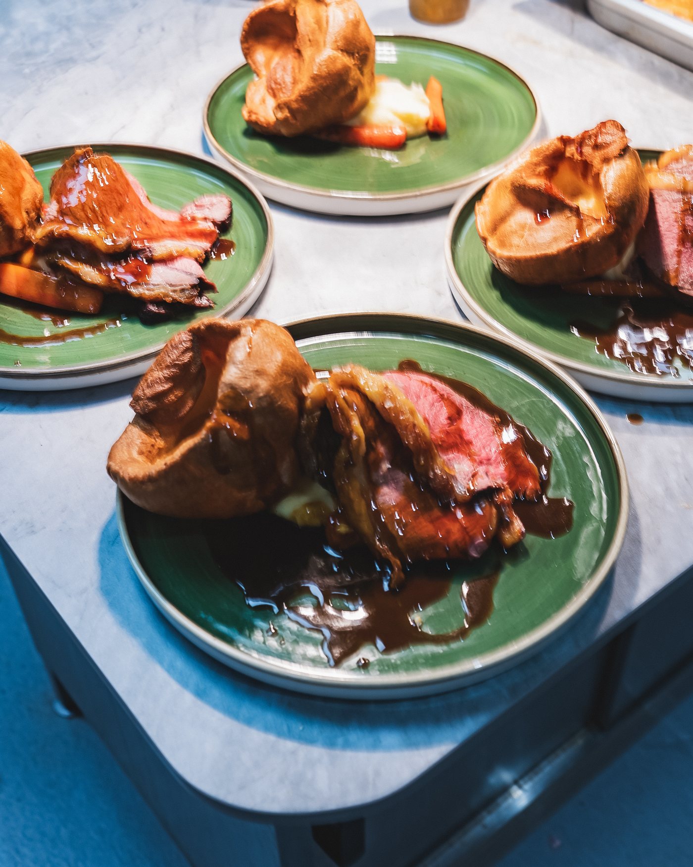 Several Sunday roasts on green plates across one table