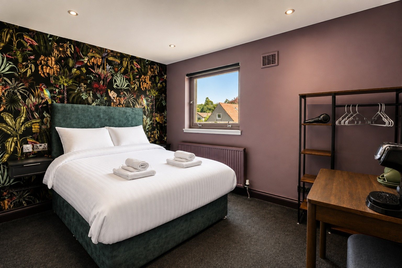 A boutique room with a writing desk, hanging rail and tea tray beside the bed