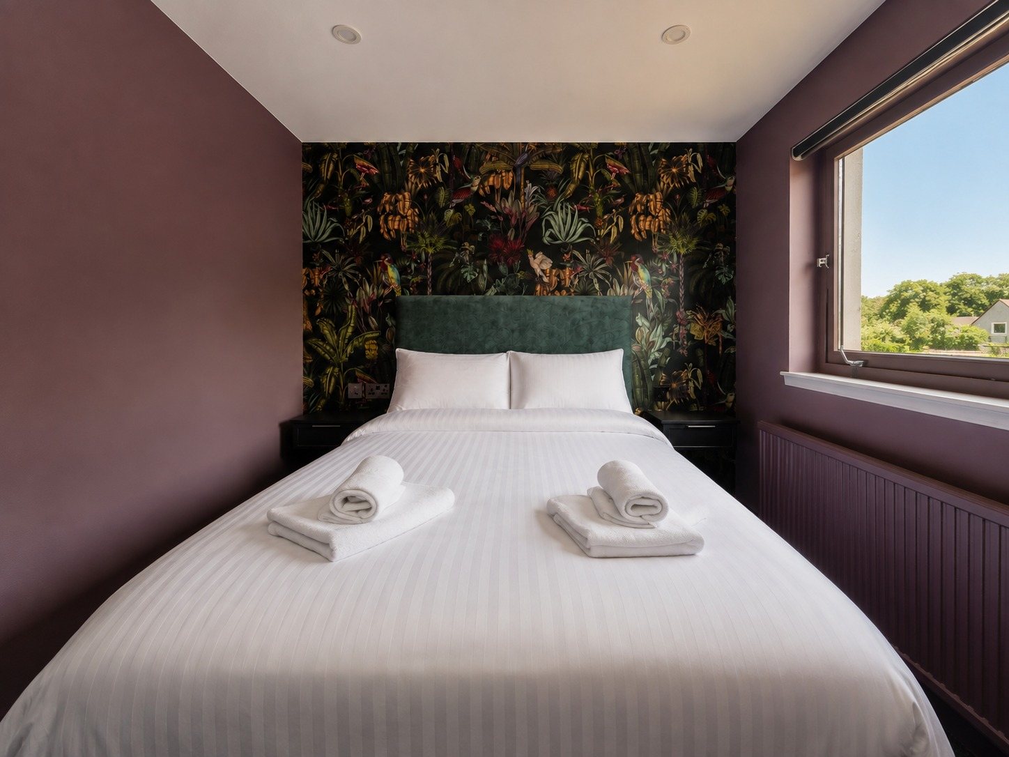A boutique room with mauve walls and botanical wallpaper, looking out over rooftops and trees