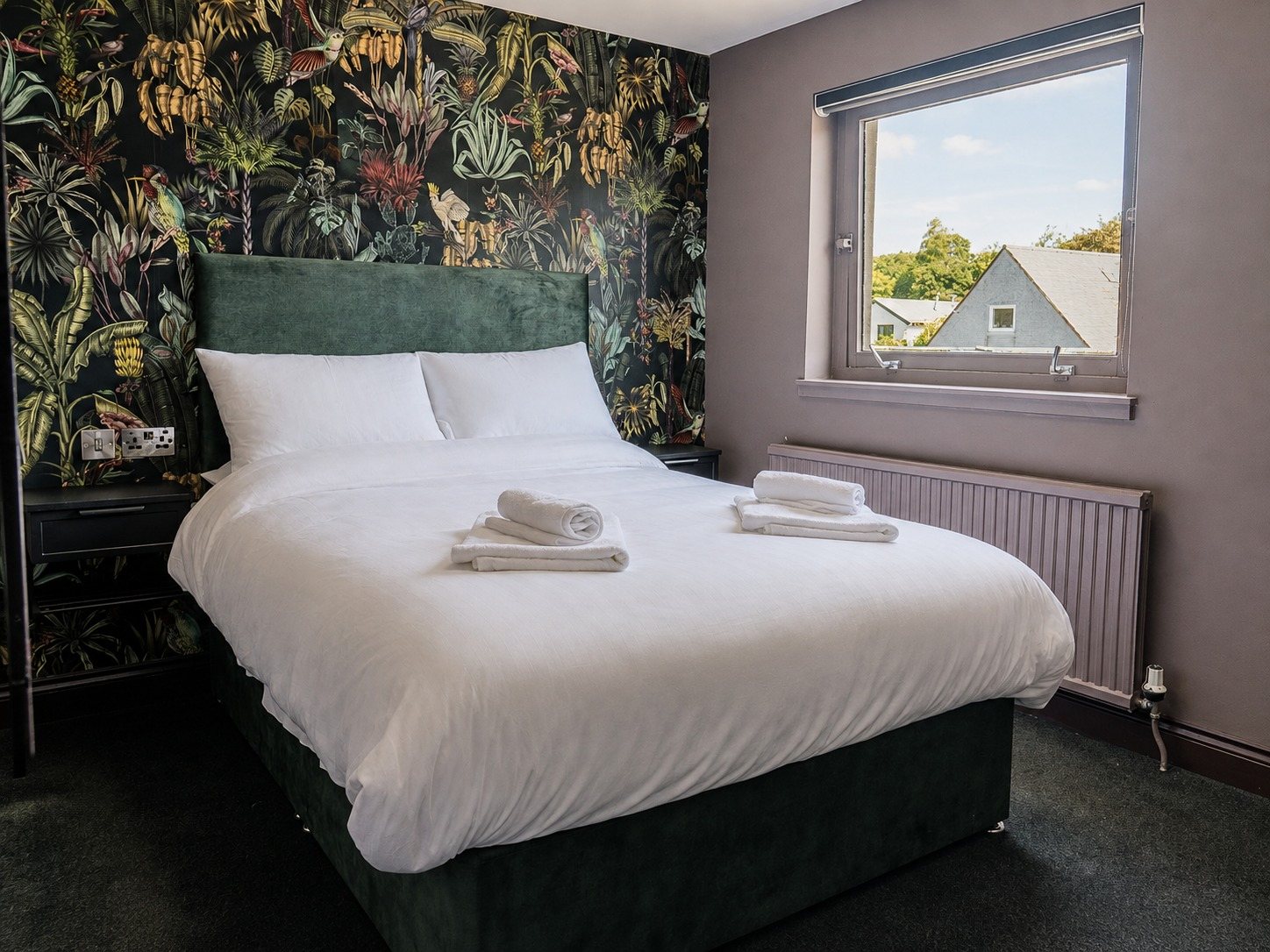 The botanical-wallpaper room with daylight coming through the window beside the bed