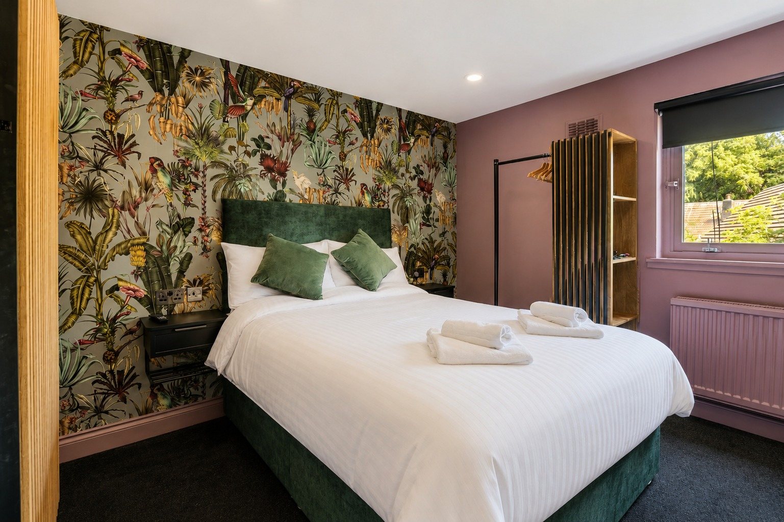 A boutique room with dusky pink walls, light botanical wallpaper and green velvet cushions
